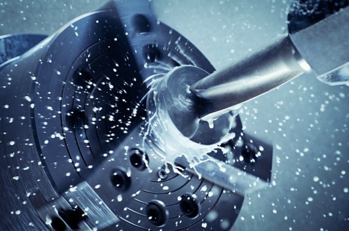 Rotating drill cutting into a metal surface, with coolant spray visible, illustrating precision machining in a manufacturing setting.