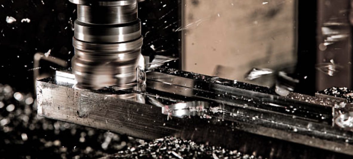 Close-up of a milling machine cutting through metal, with metal shavings flying around, highlighting precise machining in a workshop setting.